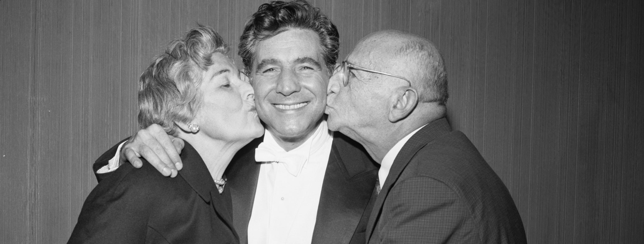 Leonard Bernstein receives kisses from his parents. (Original Caption) 1/2/1958-New York, NY: Mr. and Mrs. Samuel J. Bernstein proudly embrace their famed son, Leonard, after his first concert as conductor of the N.Y. Philharmonic Orchestra at Carnegie Hall tonight. Conductor Bernstein marked the occasion by performing as soloist in the Shostakovich Concerto No. 2 for piano and orchestra. (Credit: Getty Images / Bettmann)